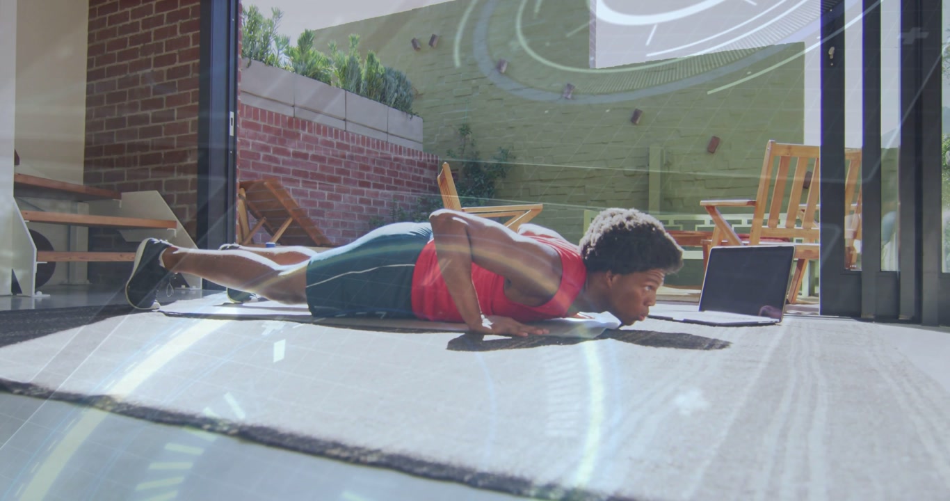 Man performing push-ups on mat facing laptop, following fitness app while HUD guiding form