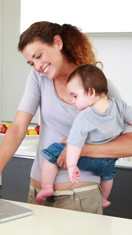 mother holding her happy baby boy and talking on phone using laptop