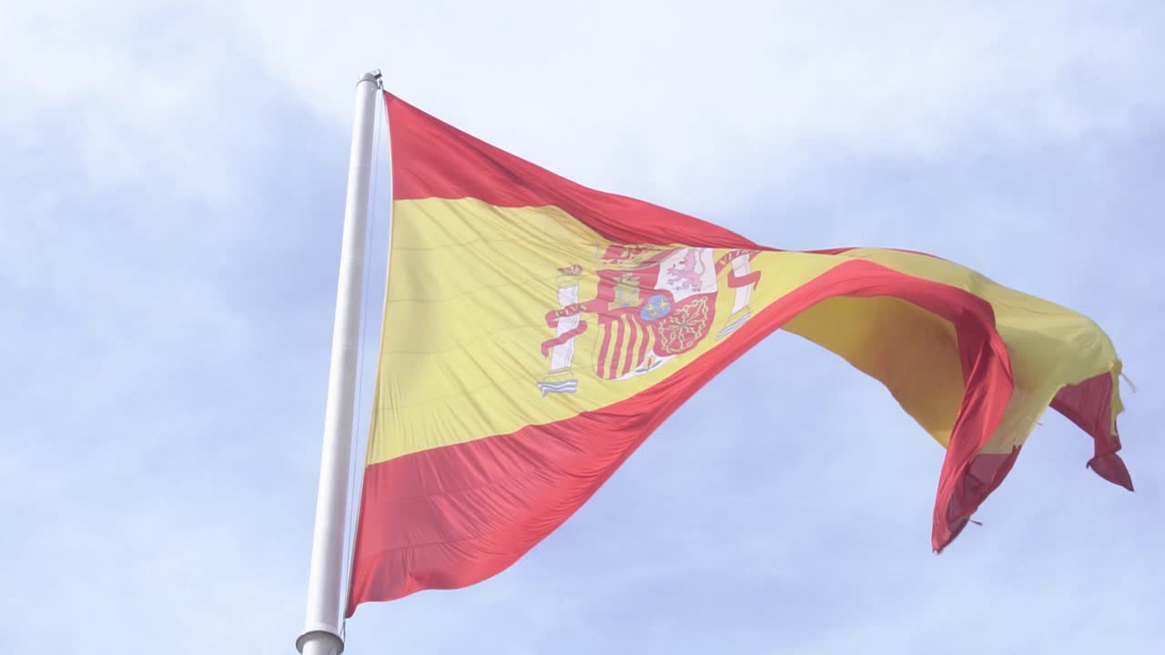 Detail shot of Spanish flag waving in the wind in slow motion with blue sky and clouds in the background close up shot of spain flag