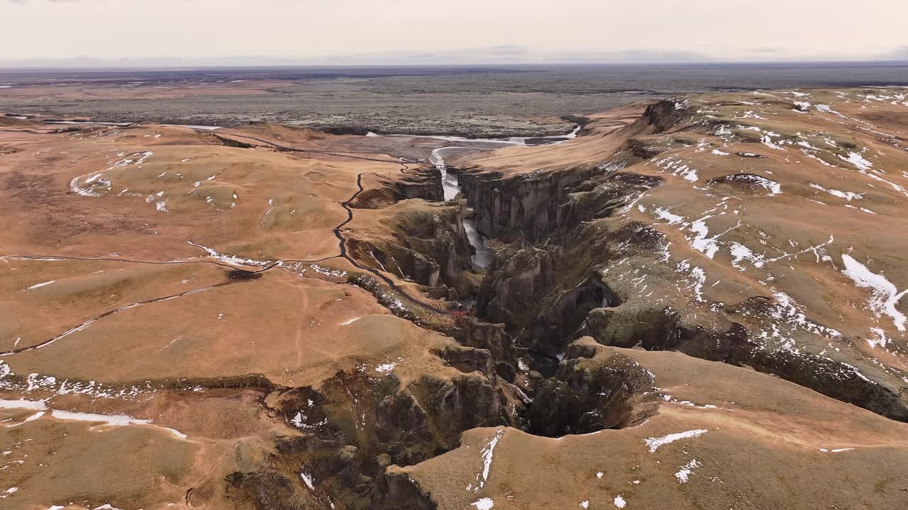 Aerial view of Fjaðrárgljúfur Canyon in Iceland, showcasing dramatic cliffs, a winding river, and a rugged, textured landscape under soft winter light.