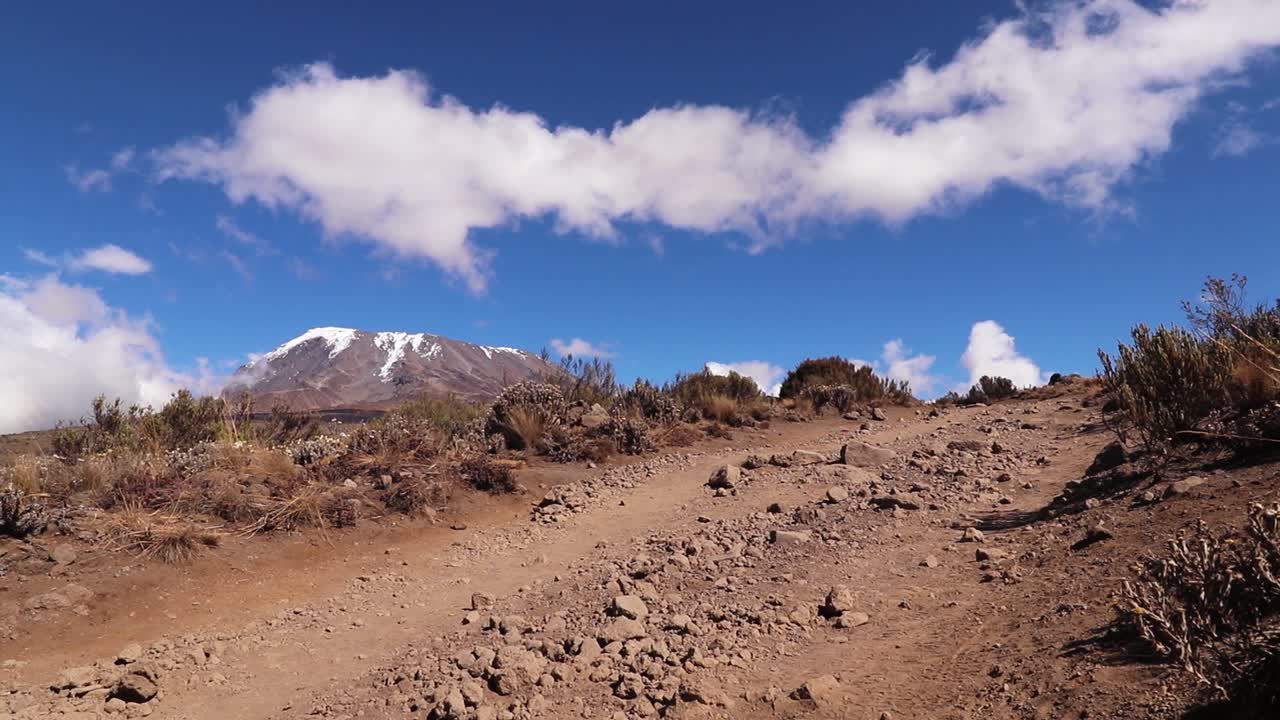 toma estática de un hombre caminando por el monte kilimanjaro, cargando cosas en la cabeza, en un día soleado, en tanzania, áfrica.