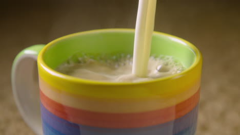 Frothy-oat-milk-is-poured-into-a-steaming-colourful-mug,-60fps