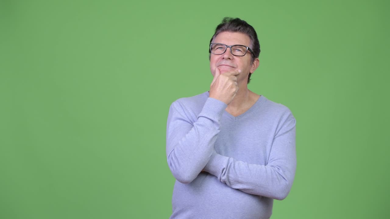 Senior handsome man thinking against green background