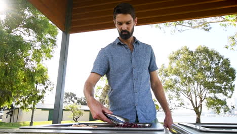 Bearded-man-cooks-vegan-food-on-hot-plate-in-park,-fixed-wide-shot