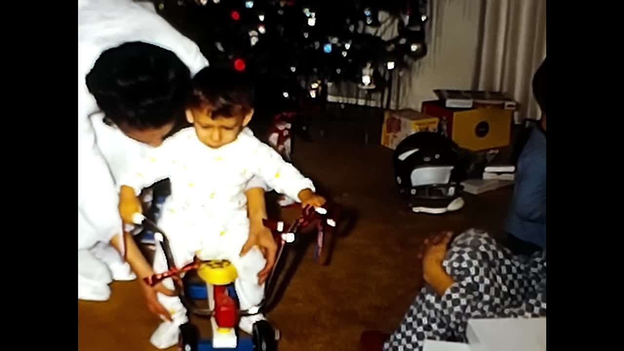 Children Playing With Tricycle in Front of Christmas Tree. CIRCA USA - 1970s: Two children enjoy playing with a tricycle in the presence of a Christmas tree in a nostalgic 1970s video from the USA.