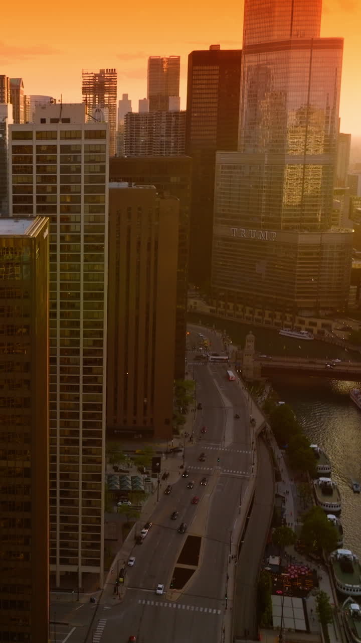 Beautiful setting sun reflecting in the mirror windows of skyscrapers. Drone flying along the roofs over Chicago River. Bright orange sky at backdrop. Vertical video