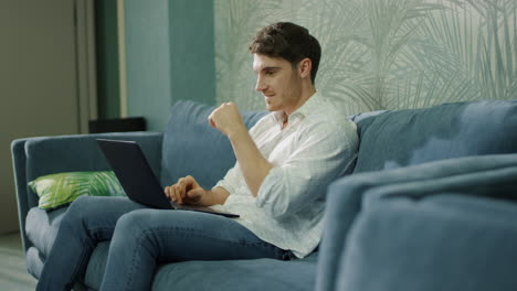 Successful-guy-receiving-message-laptop-indoors.-Happy-man-doing-winner-gesture
