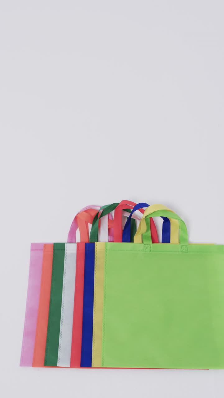 Vertical video of multi coloured canvas bags with copy space on white background