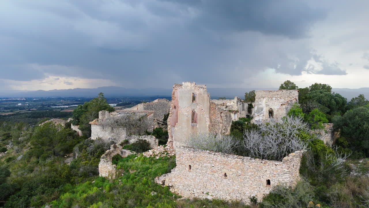 Aerial drone flight towards old stone ruins on a hill, passing overhead with dramatic storm clouds in the background