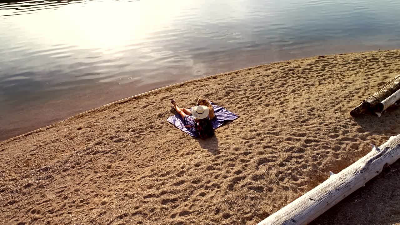 Woman with her pet dog sitting near the river coast on a sunny day 4K 4k