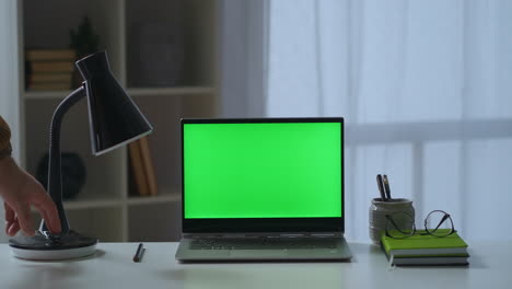 man is closing cover of laptop with green screen on table freelance and home office working place of writer or freelancer in apartment detail view on desk