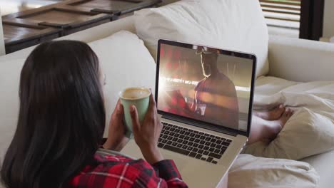 Composite-of-woman-sitting-at-home-holding-coffee-watching-sports-event-on-laptop
