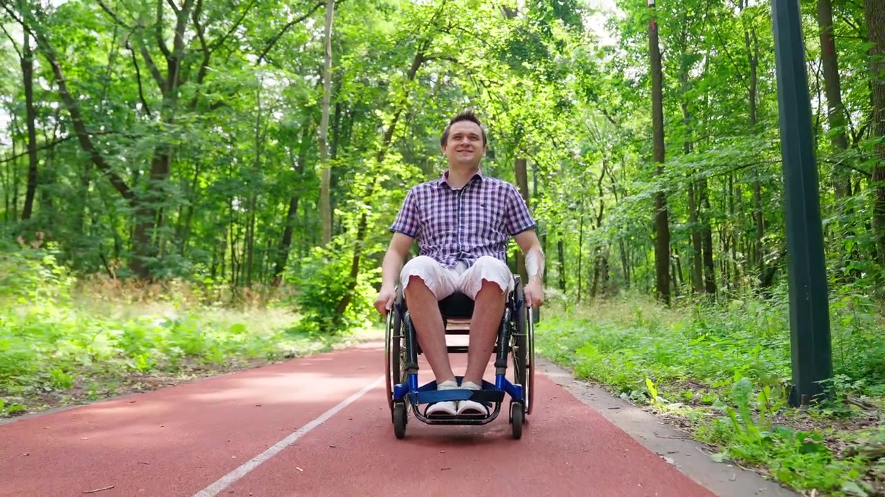 Glücklicher junger Mann im Rollstuhl sitzt auf einem Weg in einem grünen Park
