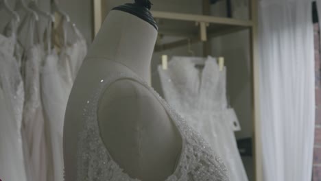 an asian woman in bright lighting adjusts a delicate, beaded wedding gown in a bridal store. the focus centers on intricate fabric details, creating an intimate, elegant atmosphere