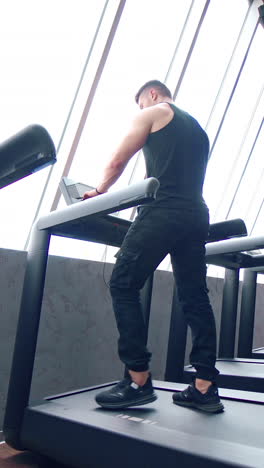 running man on treadmill machine. athletic man exercising and running on treadmill in sport gym. vertical video
