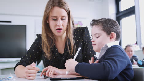 Female-teacher-working-with-a-Down-Syndrome-boy-using-a-tablet-in-a-primary-school-class,-close-up