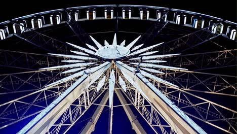 rotating illuminated ferris wheel from below with passenger gondolas suspended on the rim against a night sky at a carnival or funfair