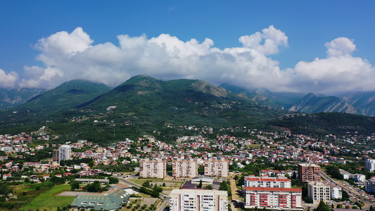 View of the city of Bar scattered at the foot of green mountains in Montenegro. White cloudscape gathering on the tops of splendid rocks.