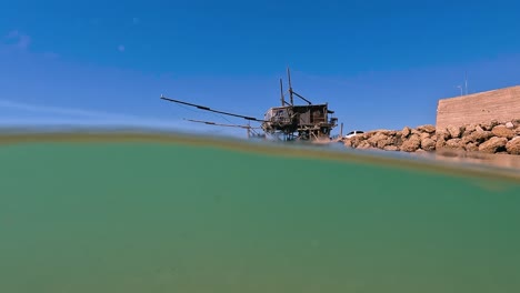 Split-over-under-underwater-view-of-trabocco-or-trabucco-at-Punta-Penna-beach-in-Costa-dei-Trabocchi-,-Abruzzo-in-Italy