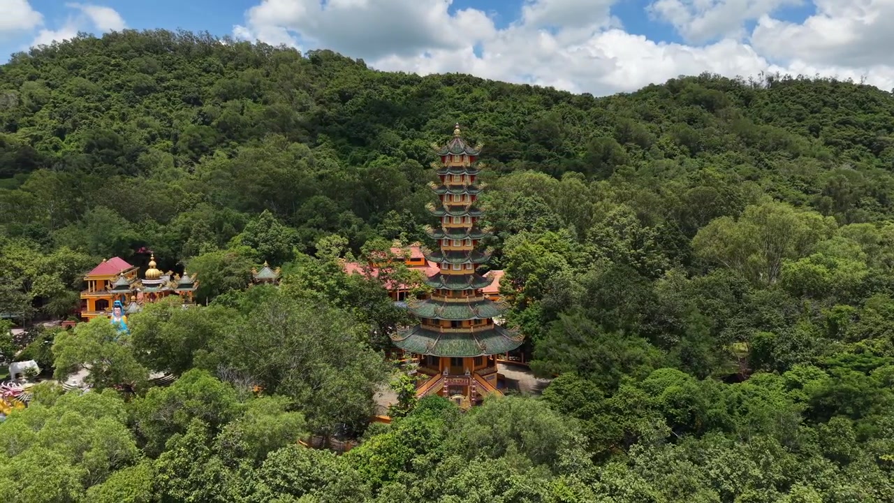 Langsom dronekredsning omkring en høj etagepagode, der står i tæt skov på en bjergside, med tempeltage og en hvid statue blandt træerne nedenfor, Tay Ninh, Vietnam