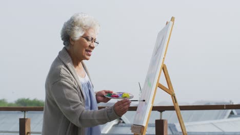 Mujer-Mayor-Afroamericana-Pintando-Sobre-Lienzo-En-El-Balcón-De-Casa