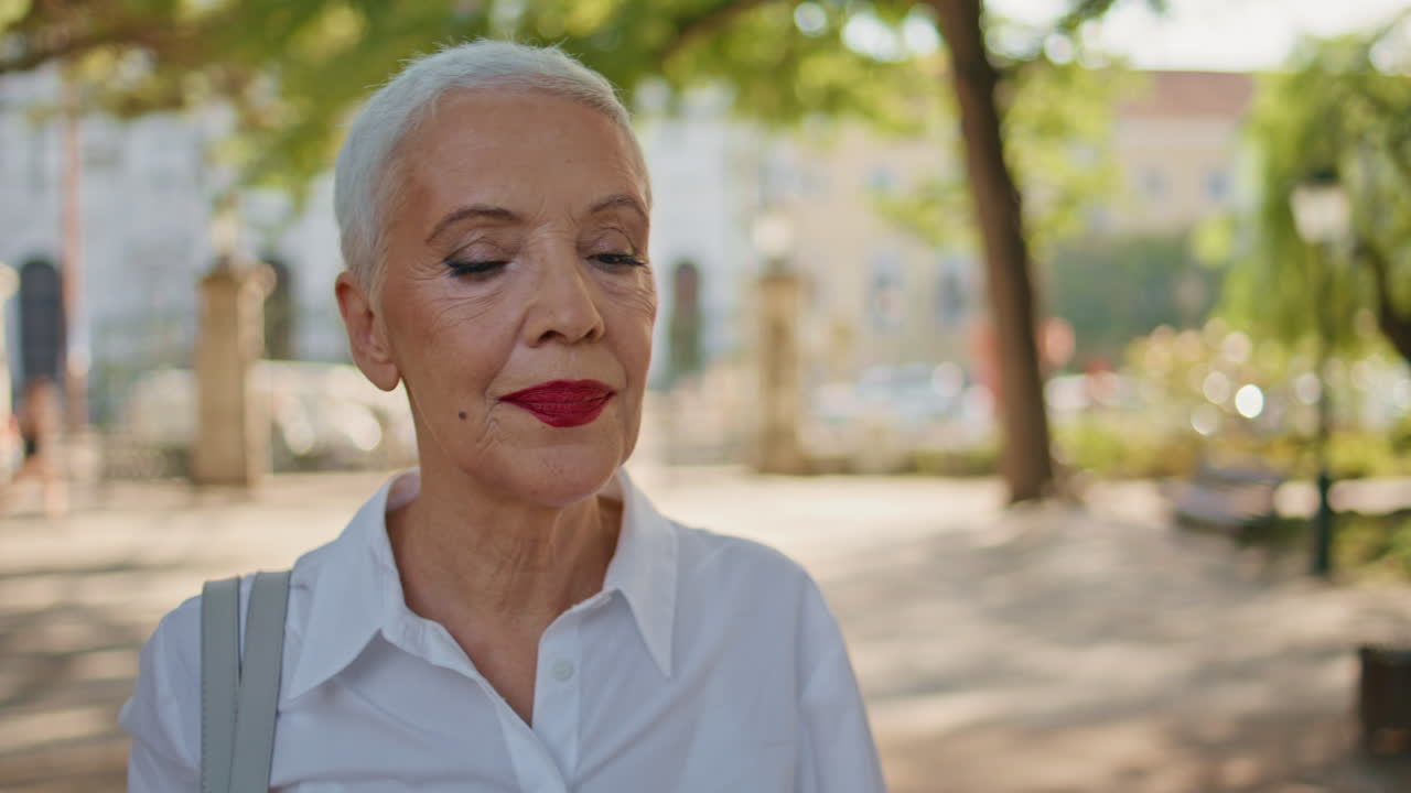 Ritratto di signora matura che va al parco urbano da sola. Anziana elegante sorridente passeggia.