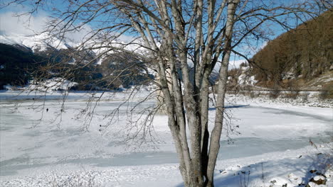 incredible orbiting aerial view of sunken bell tower in the middle of frozen lake resia with children playing and panoramic snowy mountain range