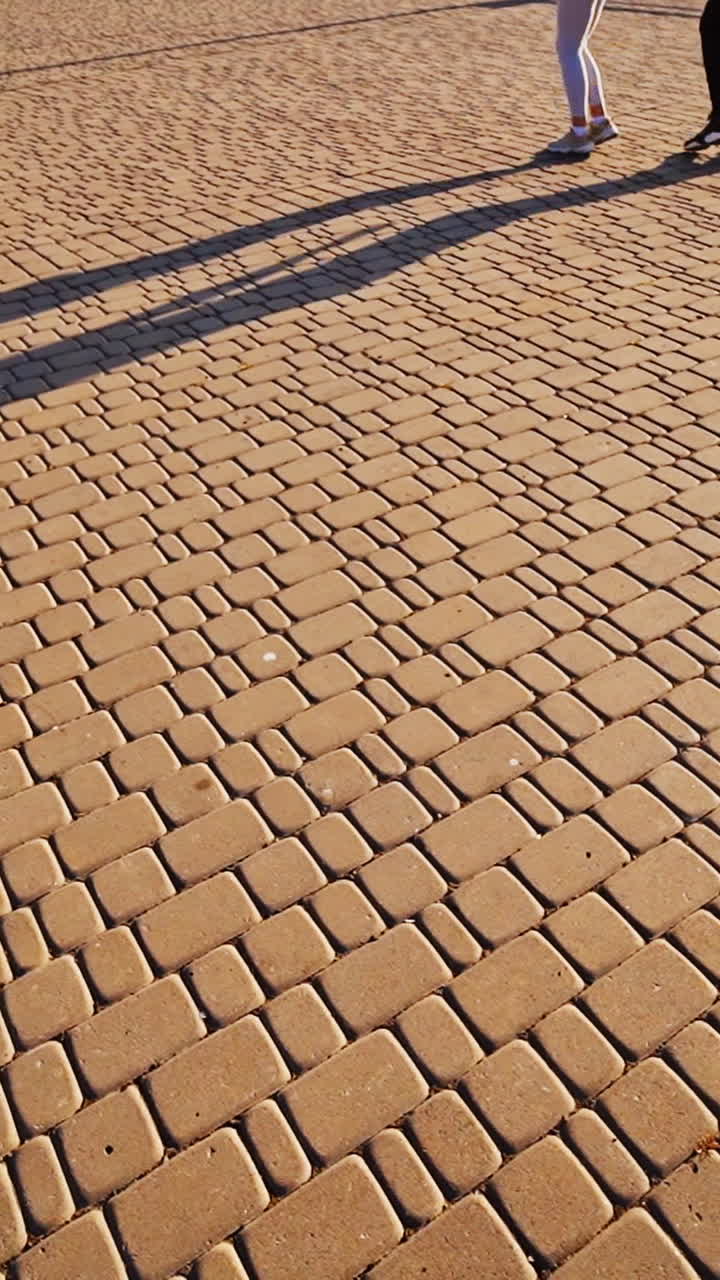 Modern dancers are dancing in the street. Urban lifestyle. Hip-hop generation. Boy's and girl's legs on the video. Paving stones and shades at sunset. Vertical video