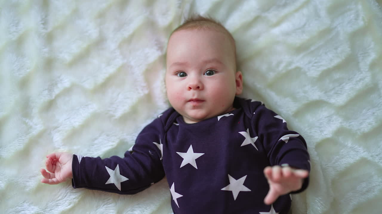 Healthy active infant boy freezes for a moment and looks straight ahead. Beautiful baby smiling slightly lying on white bed. Close up.