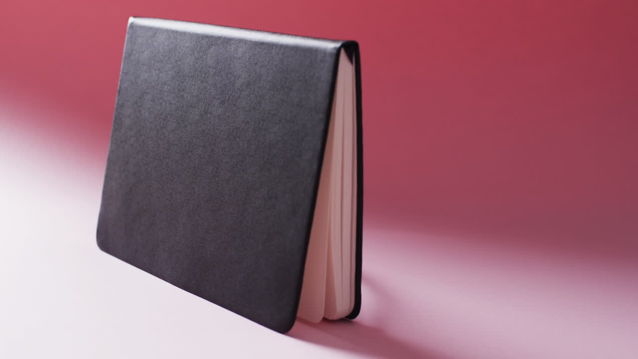 Close up of open black book standing horizontal with copy space on red background in slow motion