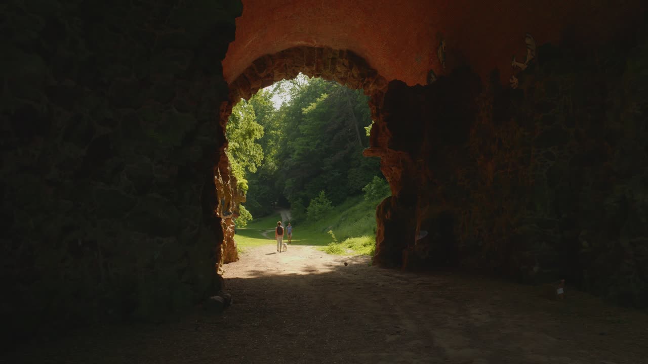 hombre caminando a través de un túnel con su perro hacia la naturaleza soleada y verde