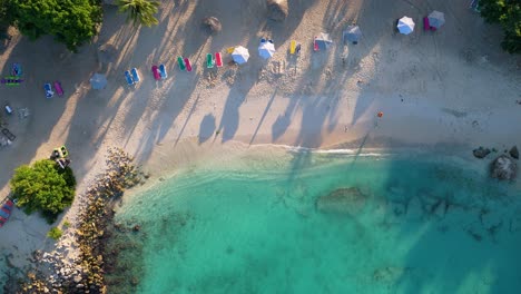 Top-down-descending-view-of-ocean-waves-crashing-on-beach-of-Curacao,-solo-person-walks-on-sand