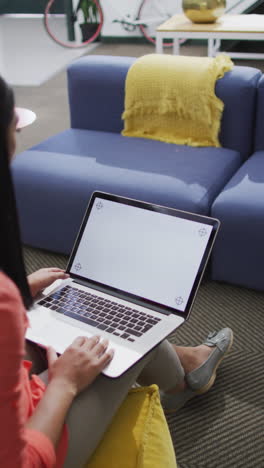 video vertical de una mujer biracial usando una computadora portátil con espacio de copia en la oficina