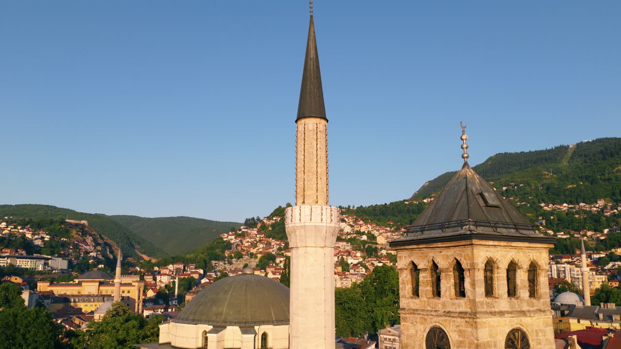 Mosque Minaret And Clock Tower With Mountains And Hillside Houses In Sarajevo At Sunset. pullback drone shot