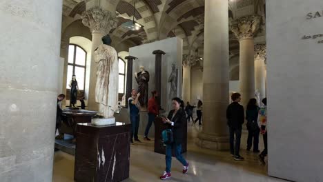 personas observando esculturas en el museo del louvre, parís