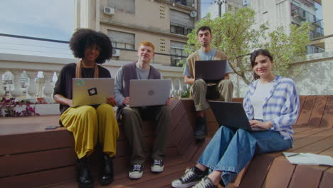 young cheerful people sitting with laptops outdoor and posing on camera