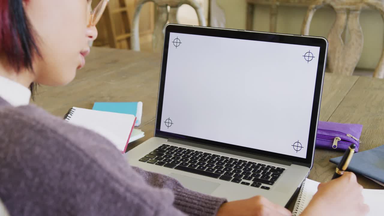 Happy biracial teenager girl sitting at table and using laptop with copy space, in slow motion
