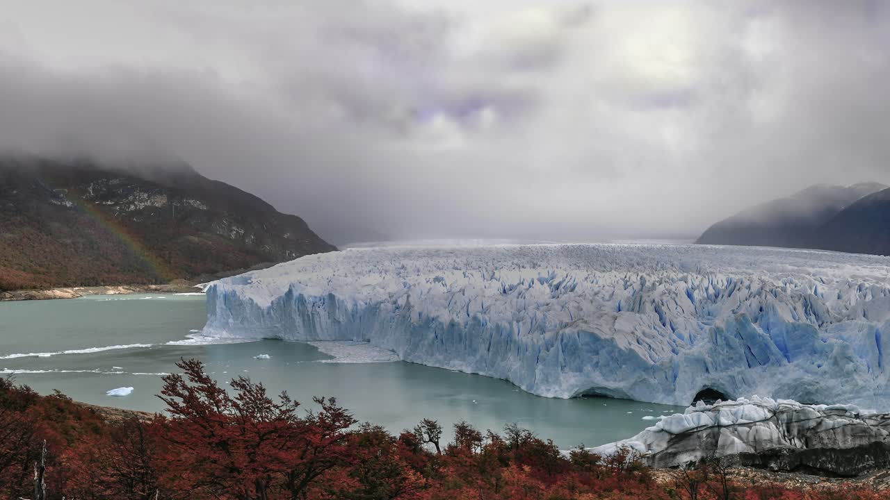 Wide panoramic scene of Perito Moreno glacier in Patagonia in autumn season with cloudy sky and rainbow in background, Argentina