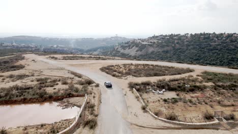 Imágenes-Aéreas-Que-Siguen-A-Un-Camión-Negro-De-Abetos-Y-Un-Lago-Sobre-Colinas-Montañosas-Durante-El-Día