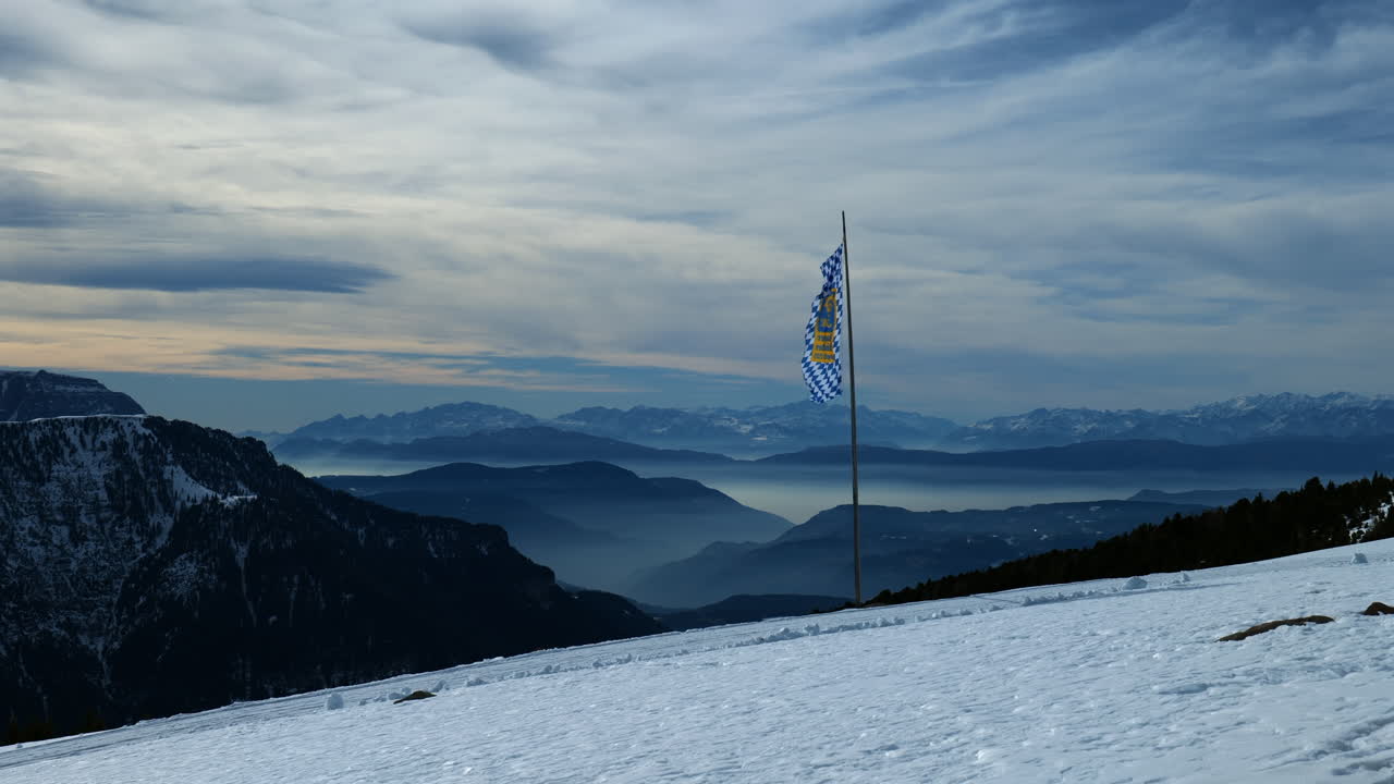 눈 인 산 들 과 황혼 에 흐릿 한 지평선 을 배경 으로 한 바이에른 국기 가 흔들리고 있다