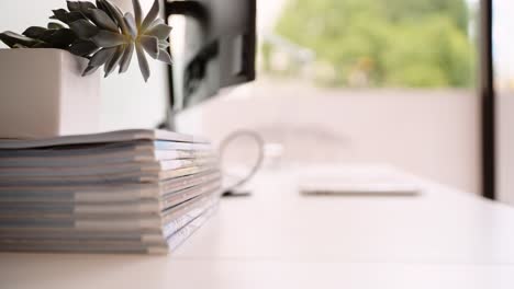 a female sitting at a white desk next to a window opening up a laptop to being working