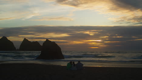 Hermosa-Puesta-De-Sol-Con-Turistas-De-Vacaciones-En-La-Orilla-Arenosa-De-La-Playa-De-La-Bahía-De-Holywell-En-Cornwall,-Inglaterra