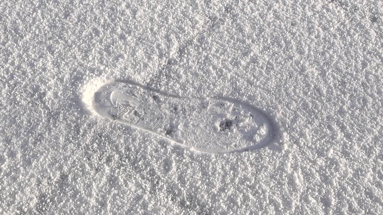 Close up view of a single footprint or shoe impression in fresh white hale or snow on ground during a sunny winter day. The trail is deep and no people are visible