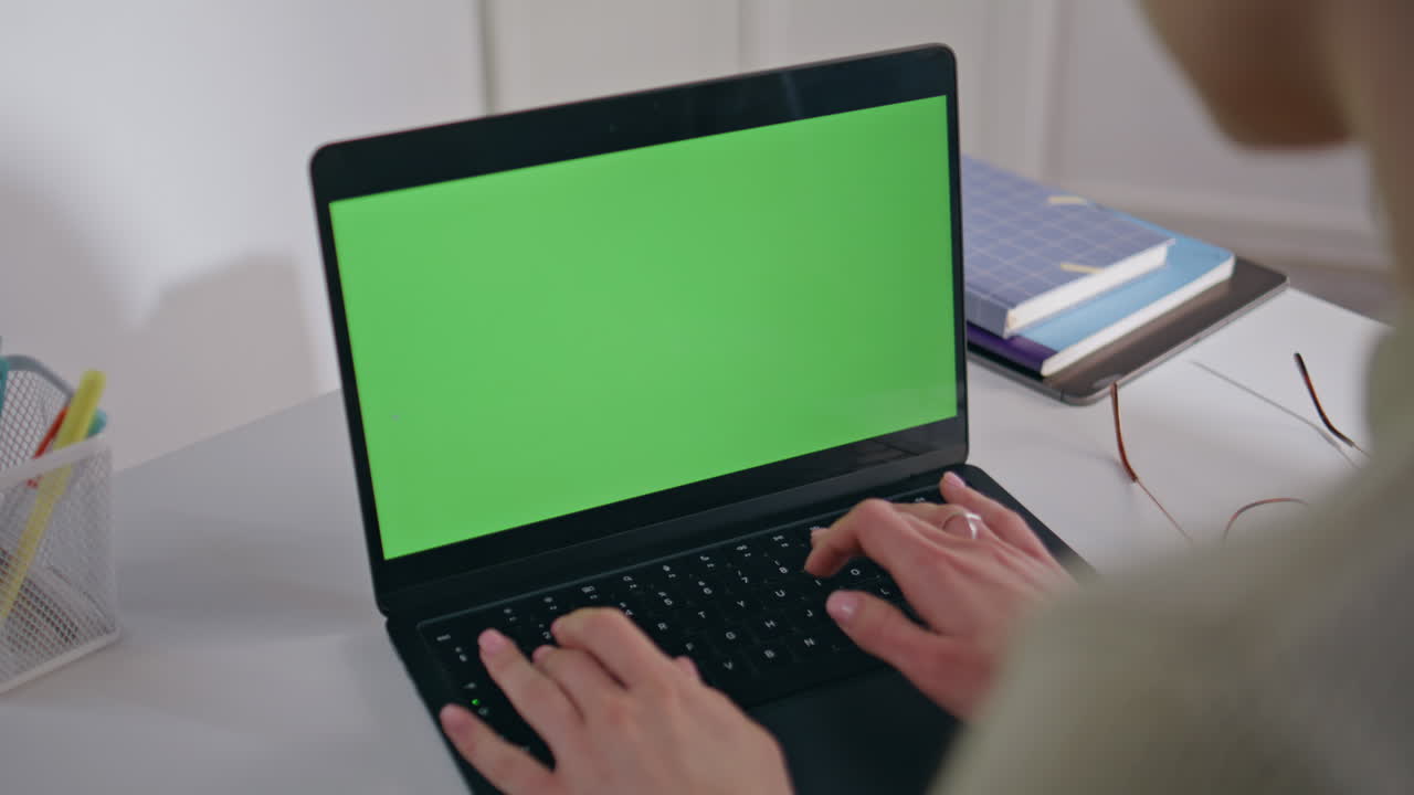 Woman hands typing greenscreen laptop keyboard at table closeup. Girl texting