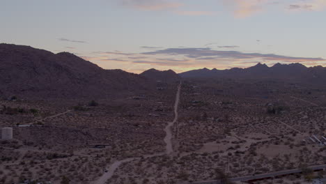 aerial push towards and over lonely dirt road heading towards the hills of joshua tree national park in california on a beautiful evening at sunset