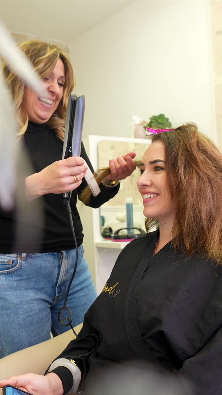 Happy Hairdresser Straightening a Woman's Hair in a Beauty Salon