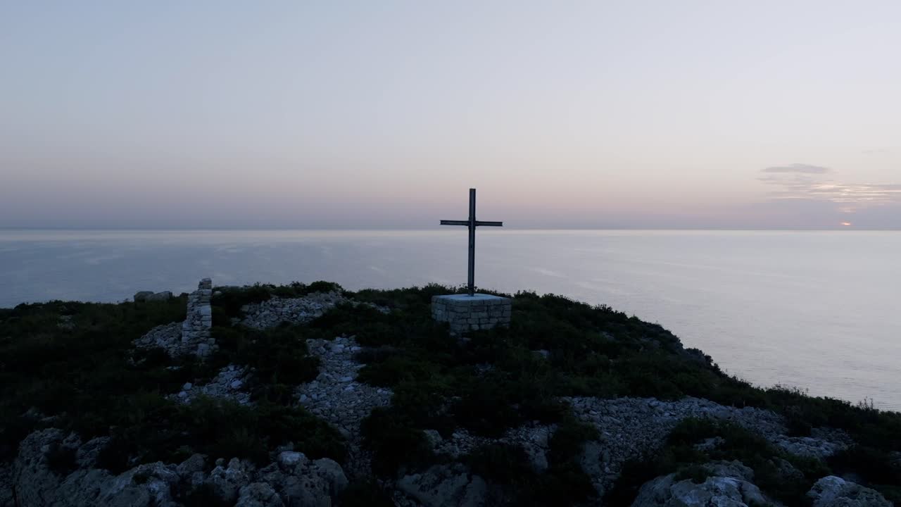 Aerial footage rotating and pulling away from a cross on the small island of Scoglio dell'Eremita in southern Italy