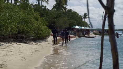 Deep-sea-fish-divers-walking-down-the-tropical-Restinga-beach-dressed-in-wet-suits-and-with-harpoons-near-the-Barra-de-Cunhaú-in-the-city-of-Canguaretama-in-the-state-of-Rio-Grande-do-Norte,-Brazil