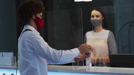 hombre de raza mixta y recepcionista llevando máscaras faciales en el mostrador de recepción del hotel