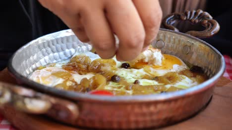 hand dipping bread into delicious fried eggs with onions in a traditional copper pan